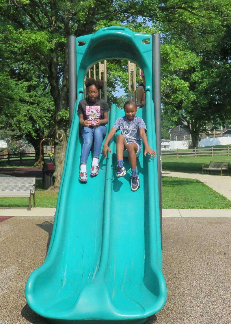 A Little Girl Sliding Down A Green Slide At The Playground. by